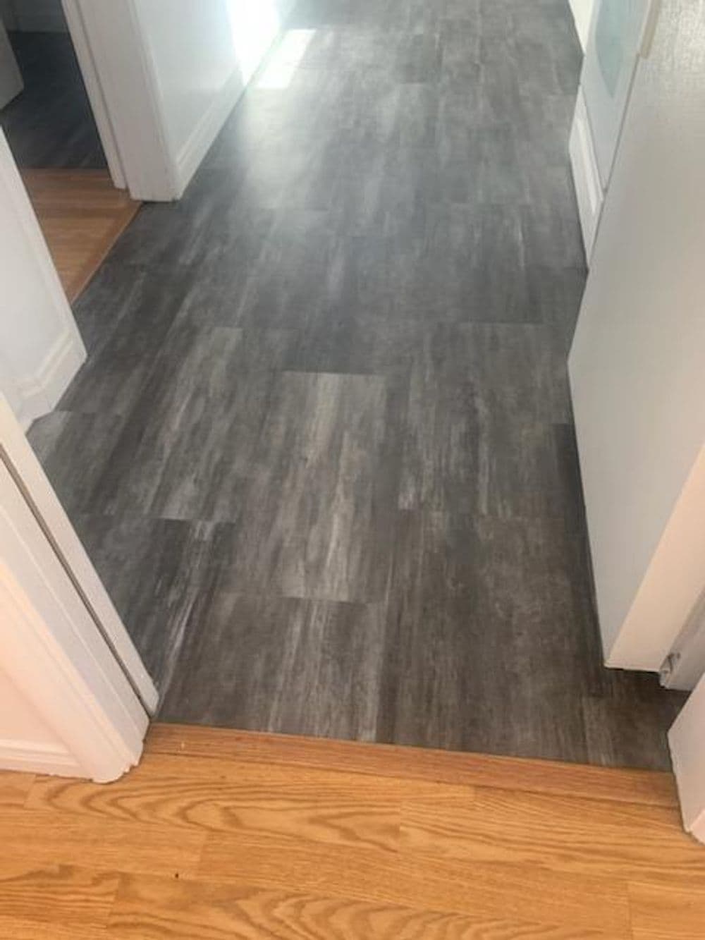 Gray vinyl flooring transitioning to wooden floor in a hallway. Modern and stylish interior design.
