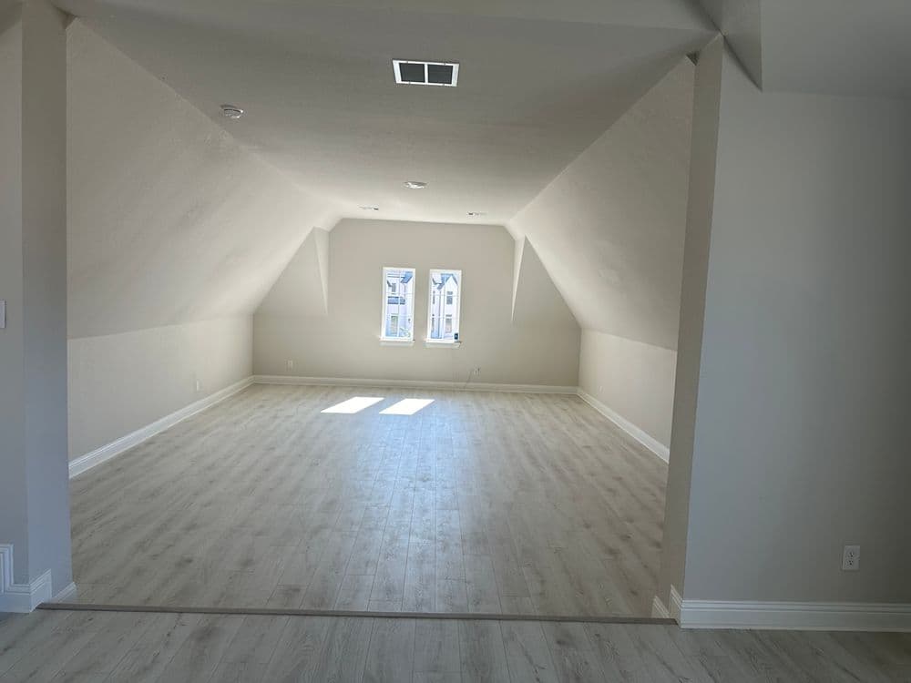 Spacious empty attic with natural light, wood-like flooring, and sloped ceiling.