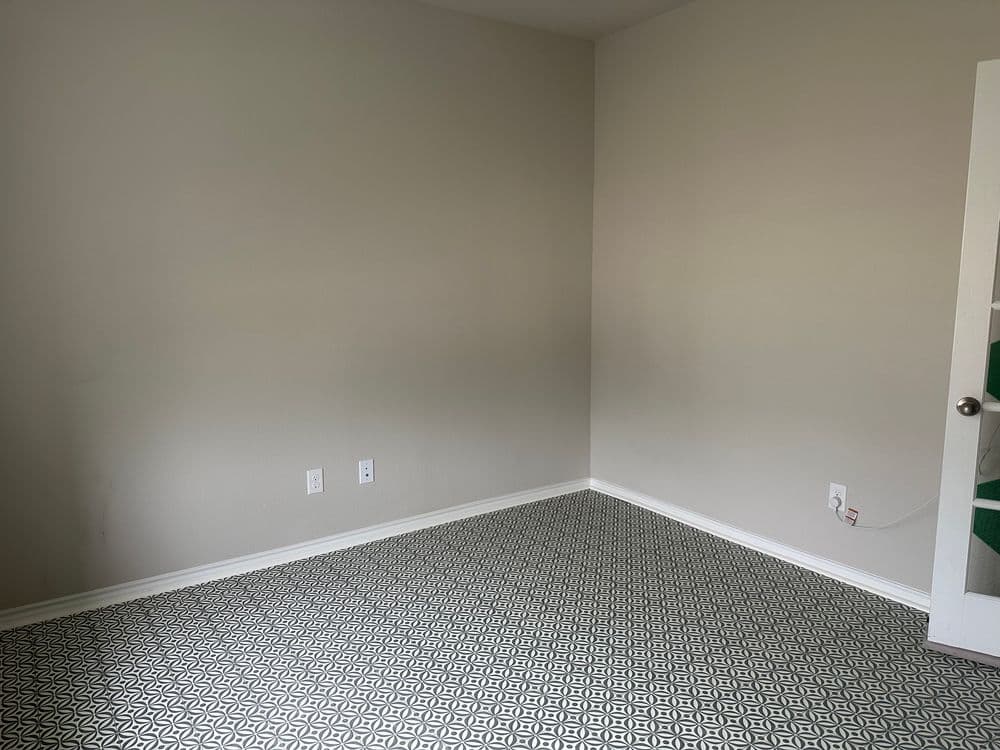 Empty room with light gray walls and patterned black and white floor tiles.