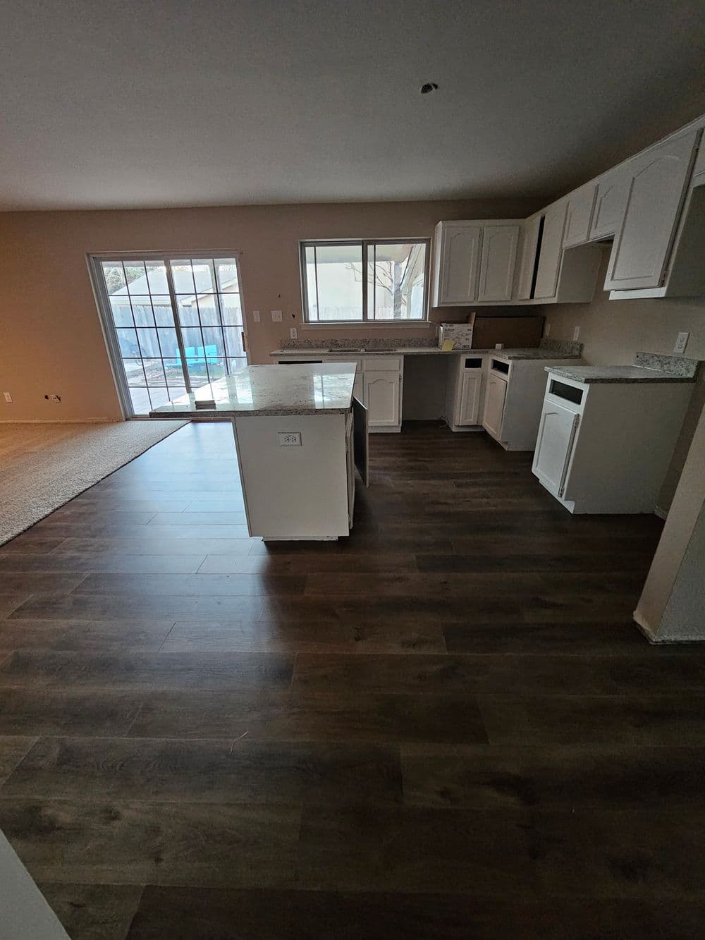 Modern kitchen with white cabinets, granite countertops, and open layout leading to a patio.