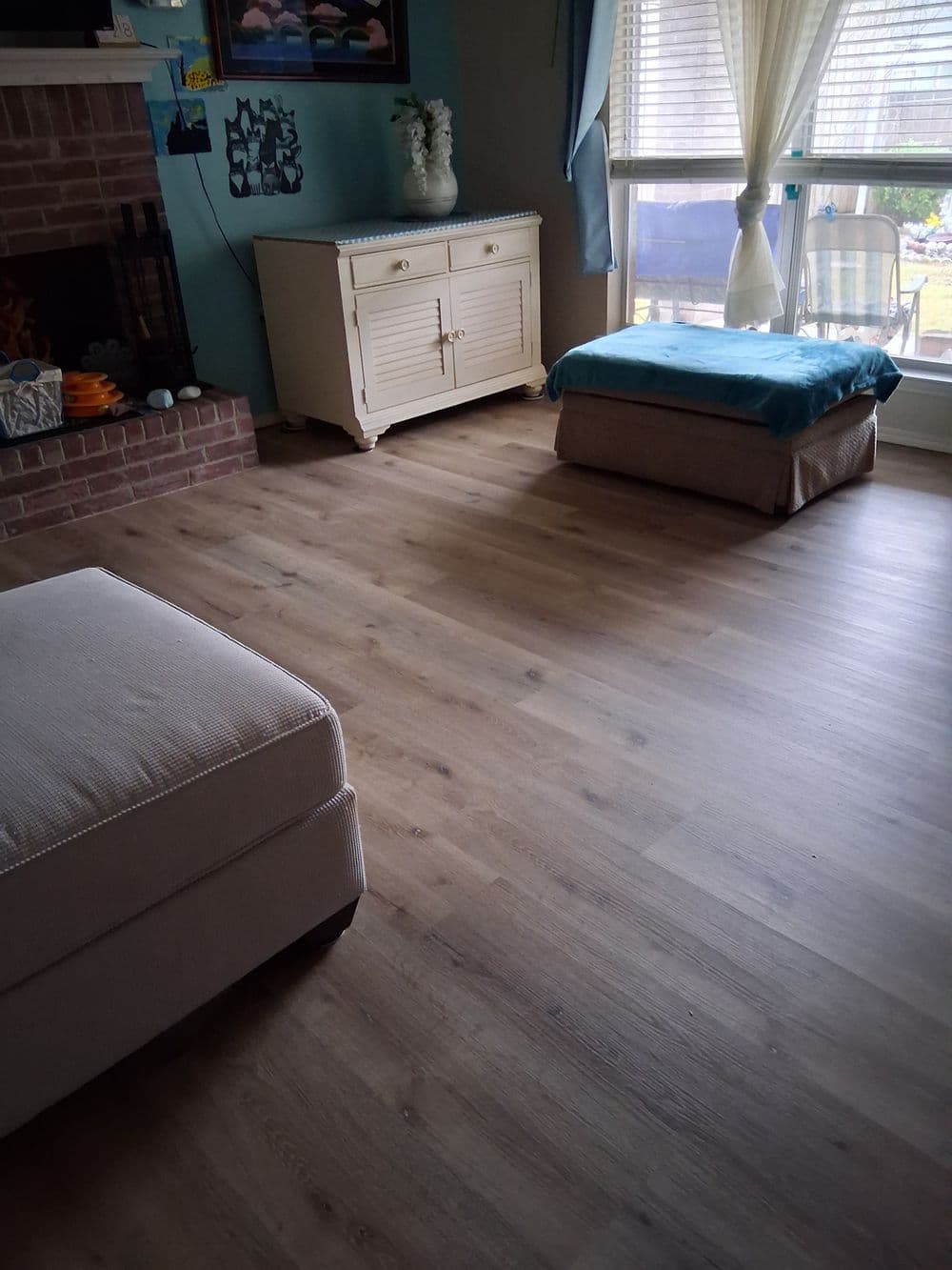 Cozy living room with light wood flooring, beige sofa, and a white cabinet by a sunny window.