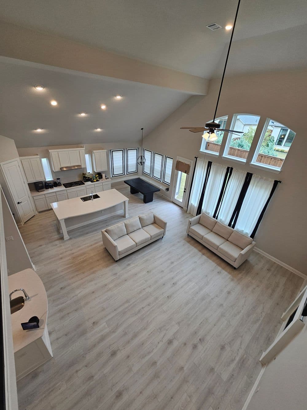 Spacious modern living room with white furniture, high ceilings, and large windows.