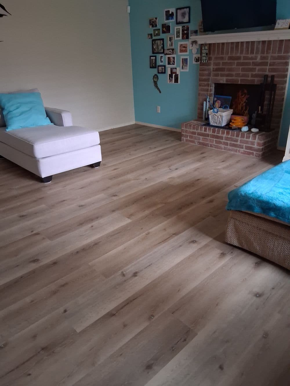 Cozy living room with hardwood floors, a fireplace, a white chair, and teal accents.