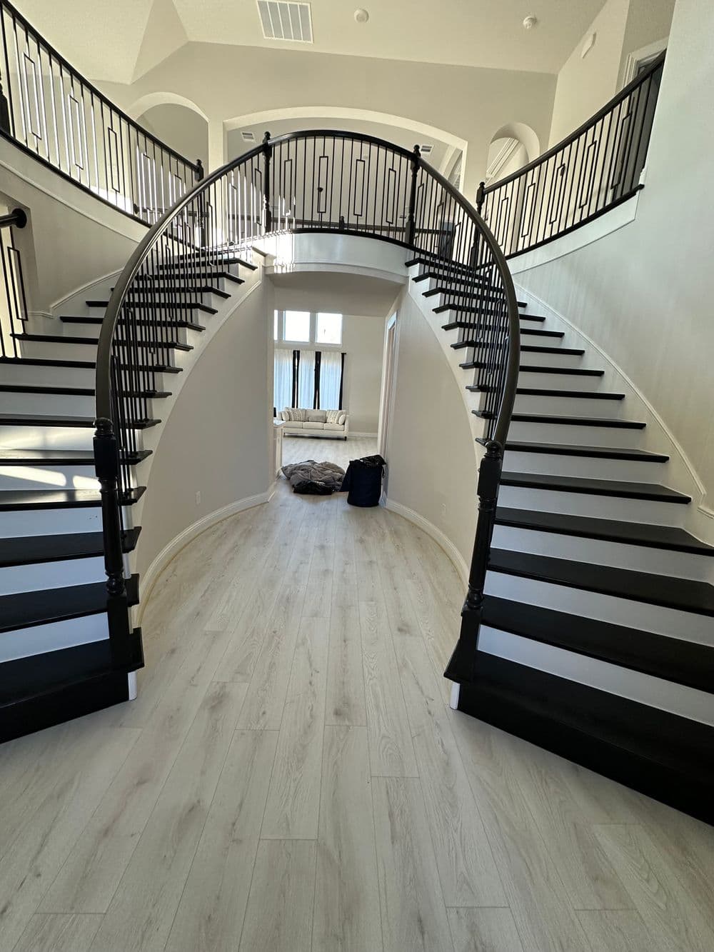 Elegant foyer with double curved staircases and light wood flooring in a modern home.