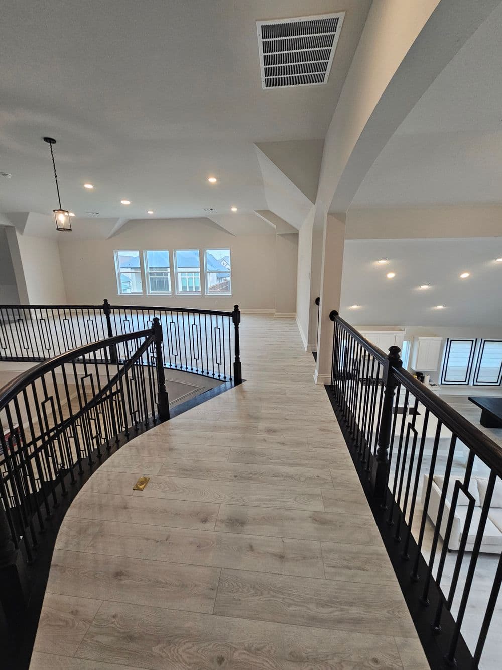 Spacious modern interior with curved staircase and large windows, featuring light wood flooring.