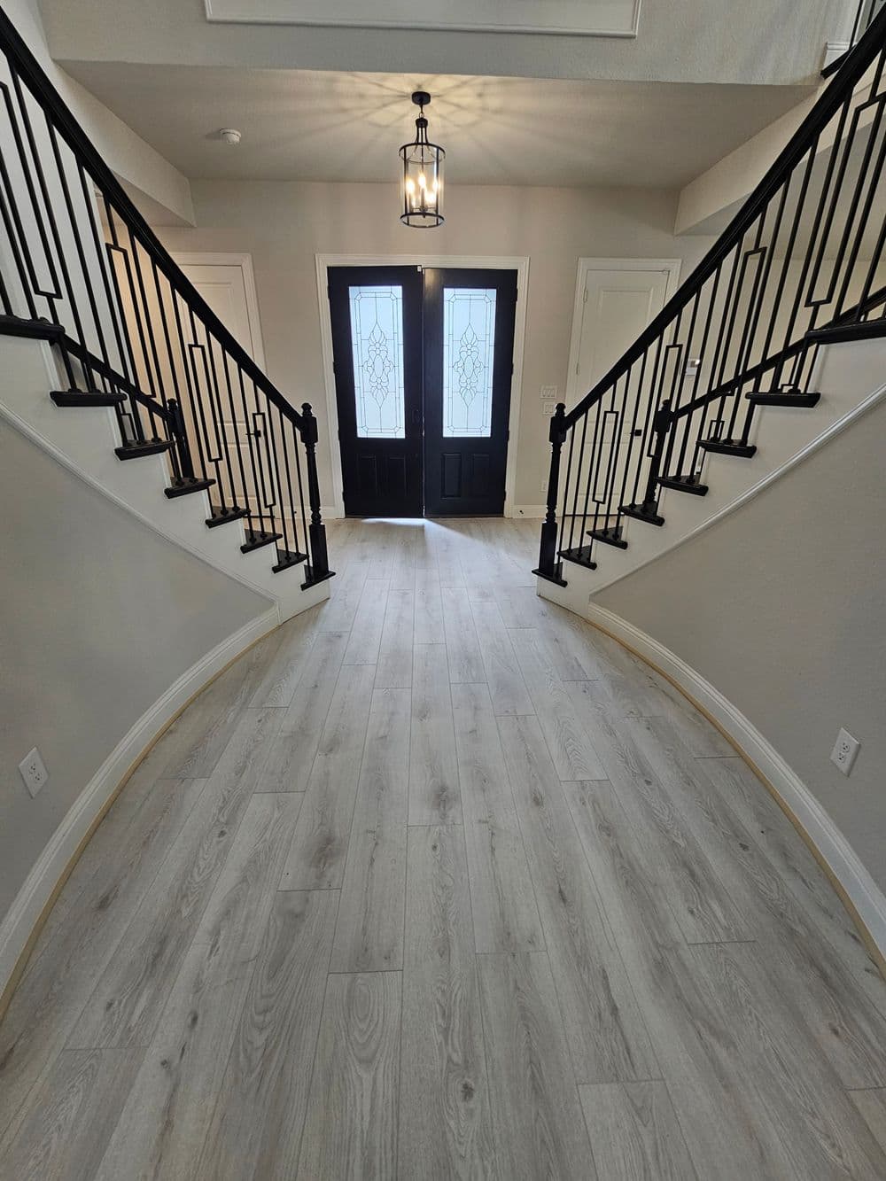 Elegant foyer with curved staircase, wood flooring, and double black front doors.