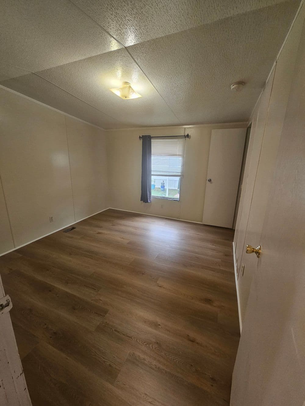 Empty interior of a room with light-colored walls and wooden flooring, featuring a window.