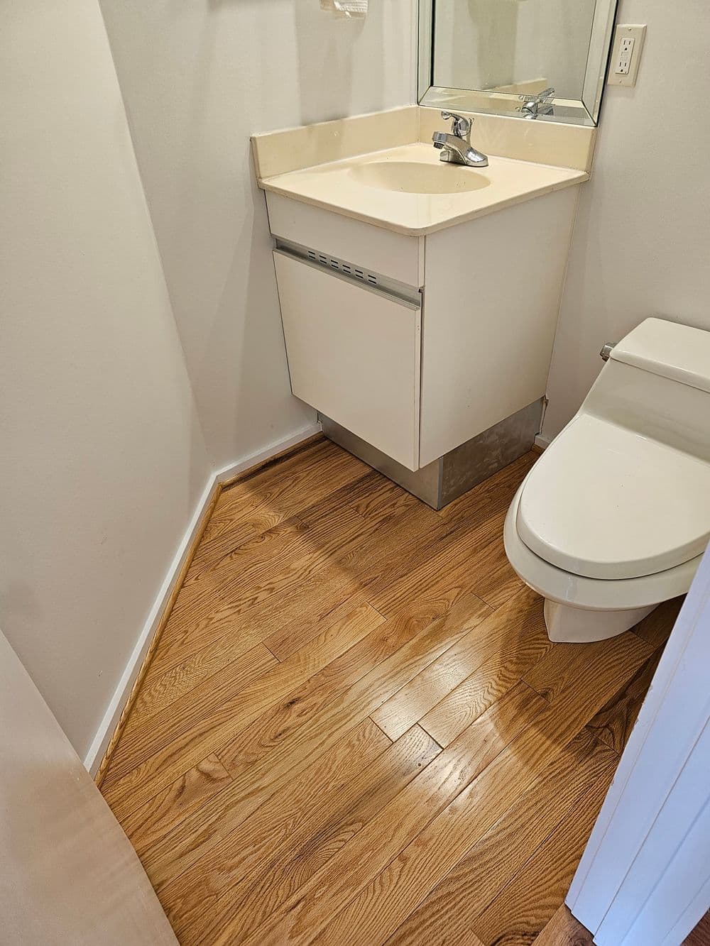 Small bathroom with hardwood floor, modern sink, and toilet, featuring clean lines and natural light.
