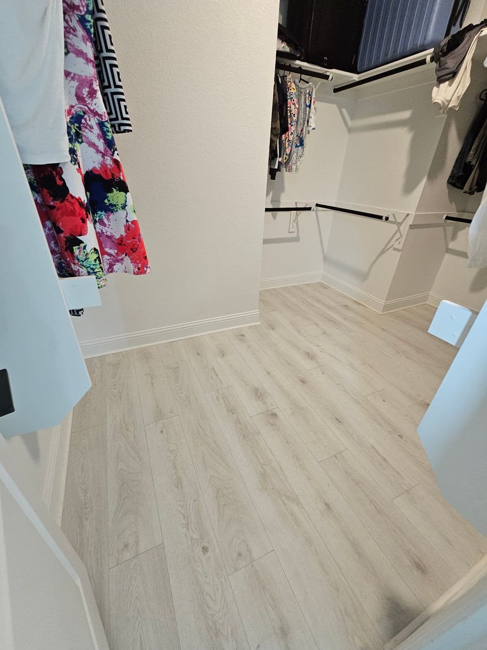 Spacious walk-in closet with light wood flooring and organized clothing racks.