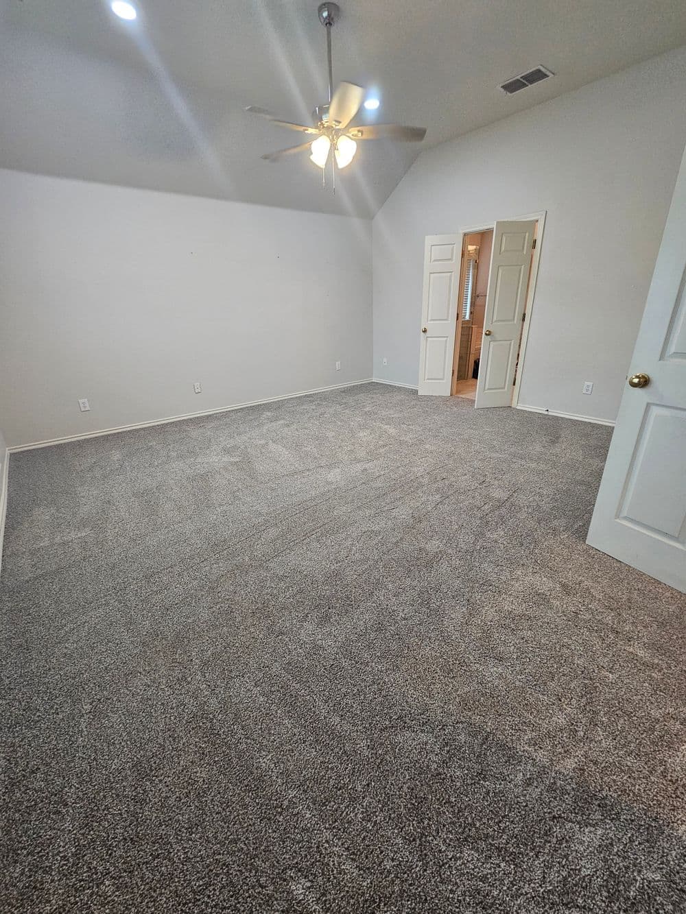 Spacious bedroom with ceiling fan, carpeted flooring, and light-colored walls.