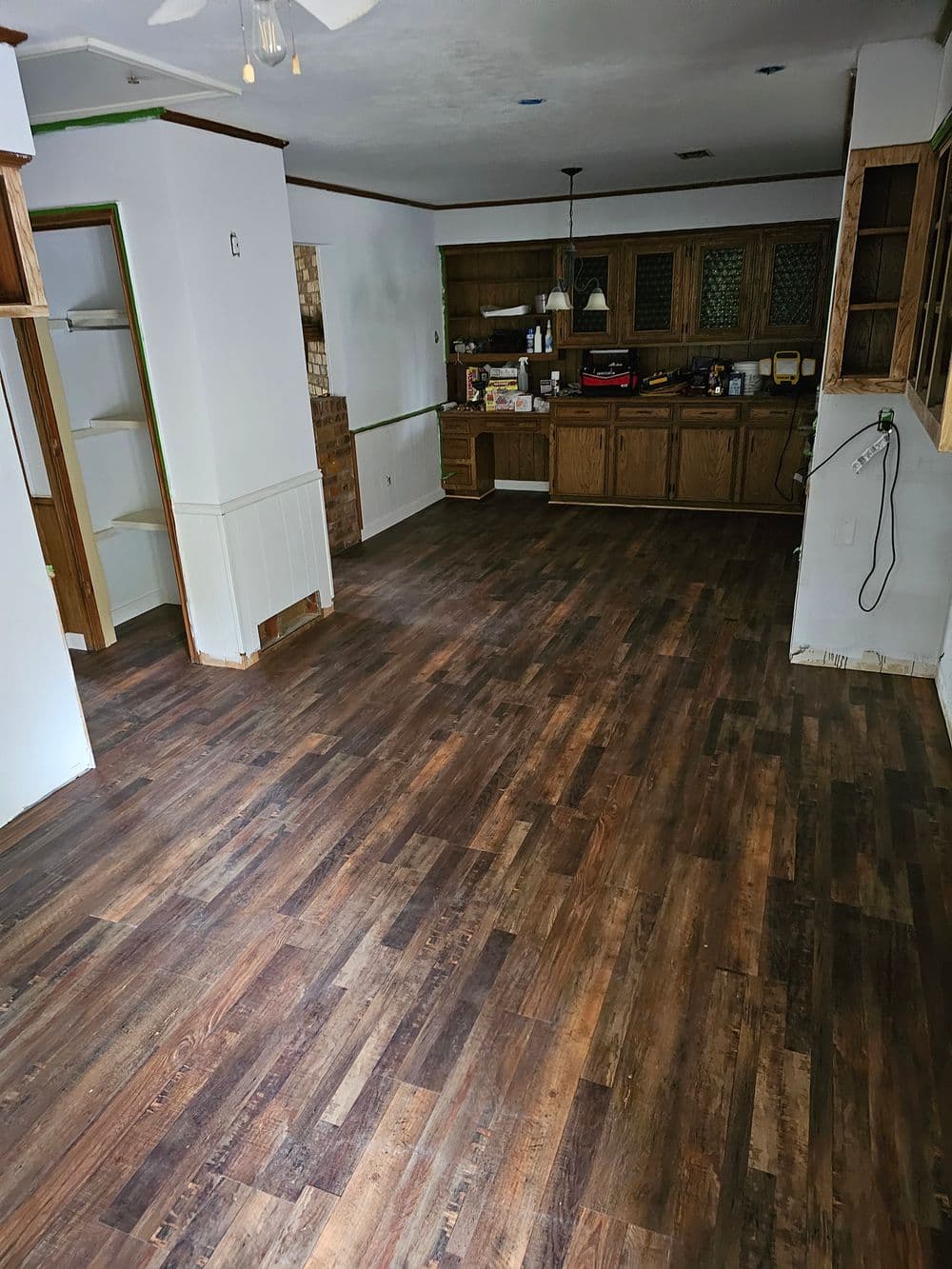 Empty kitchen with wooden flooring and cabinets, showcasing a spacious layout and natural light.