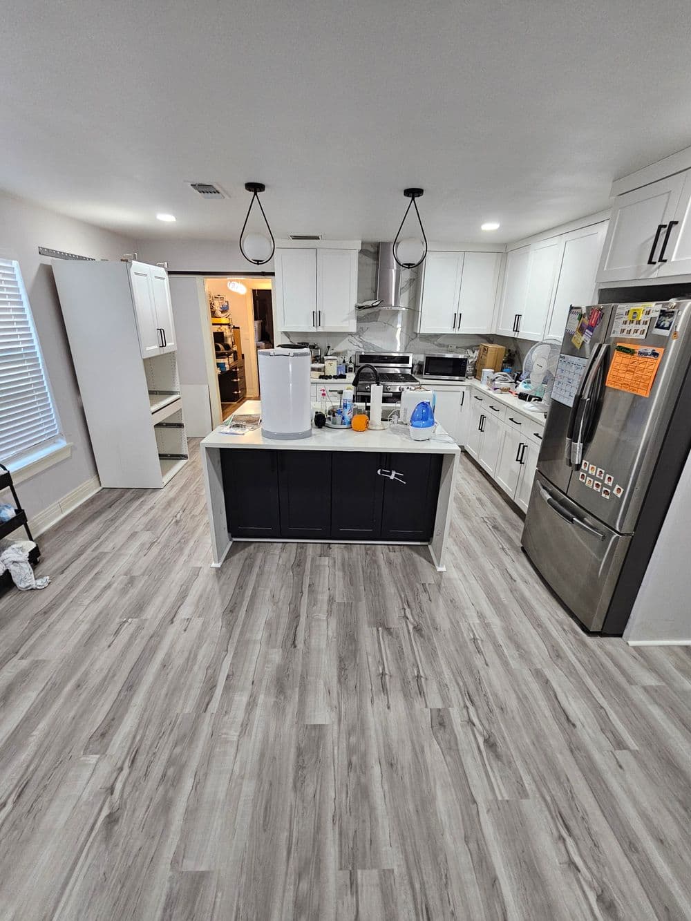 Modern kitchen with white cabinets, stainless steel appliances, and wood-style flooring.