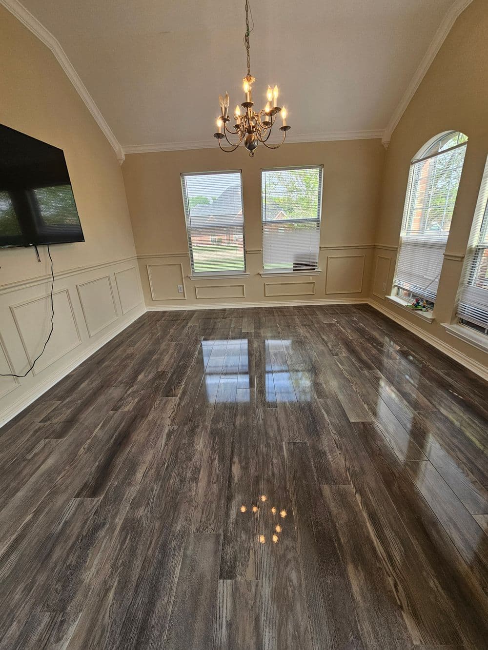 Spacious living room with chandelier, large windows, and glossy hardwood flooring.