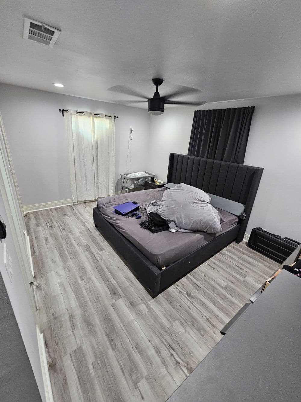 Modern bedroom interior with a messy bed, wooden flooring, and natural light from a window.