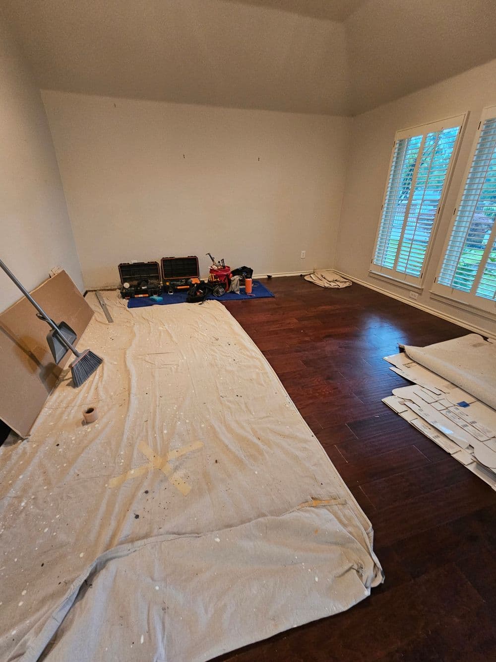Empty room with wooden floor, covered with a tarp and construction tools on the side.