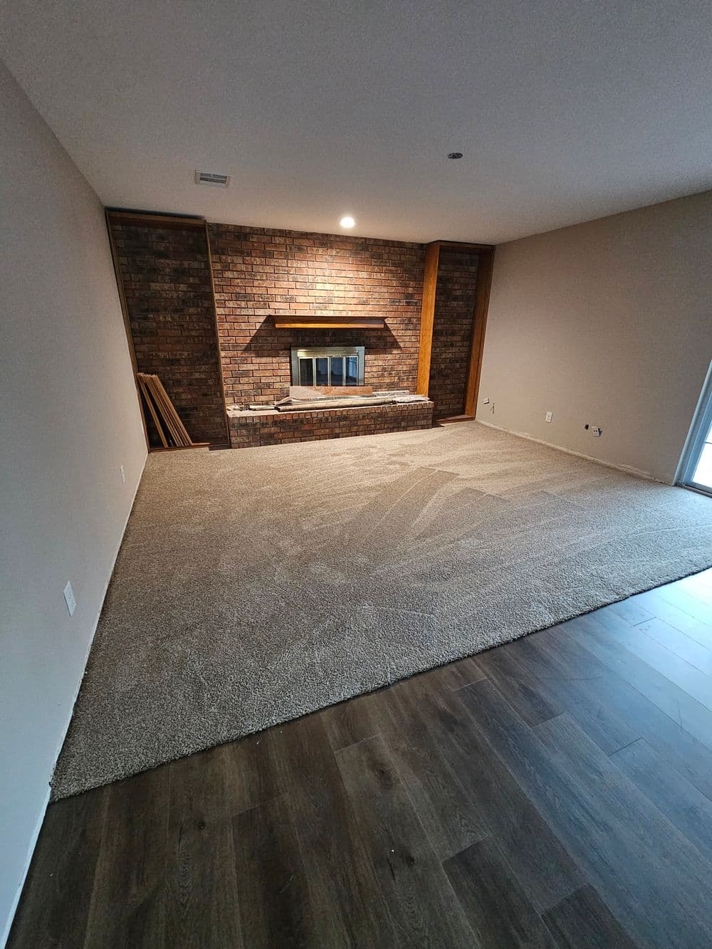 Spacious living room with brick fireplace, fresh carpet, and hardwood floors. Natural light streaming in.