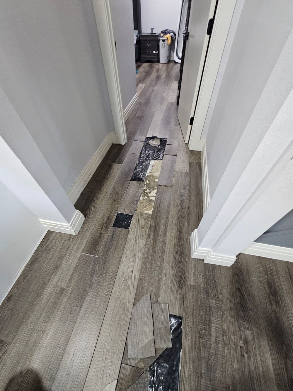 Repairing damaged laminate flooring in a hallway with wooden tiles and black patches visible.
