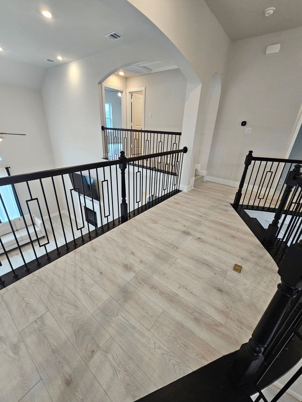 Modern interior balcony with black railings and light wood flooring in a spacious home.