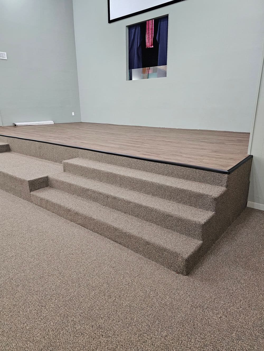 Carpeted stage with five steps, set in a neutral wall interior and a display screen backdrop.