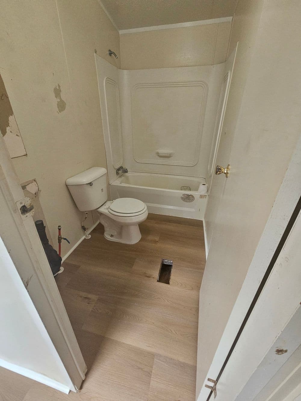 Small bathroom featuring a toilet, bathtub, and wooden flooring with an unfinished area.