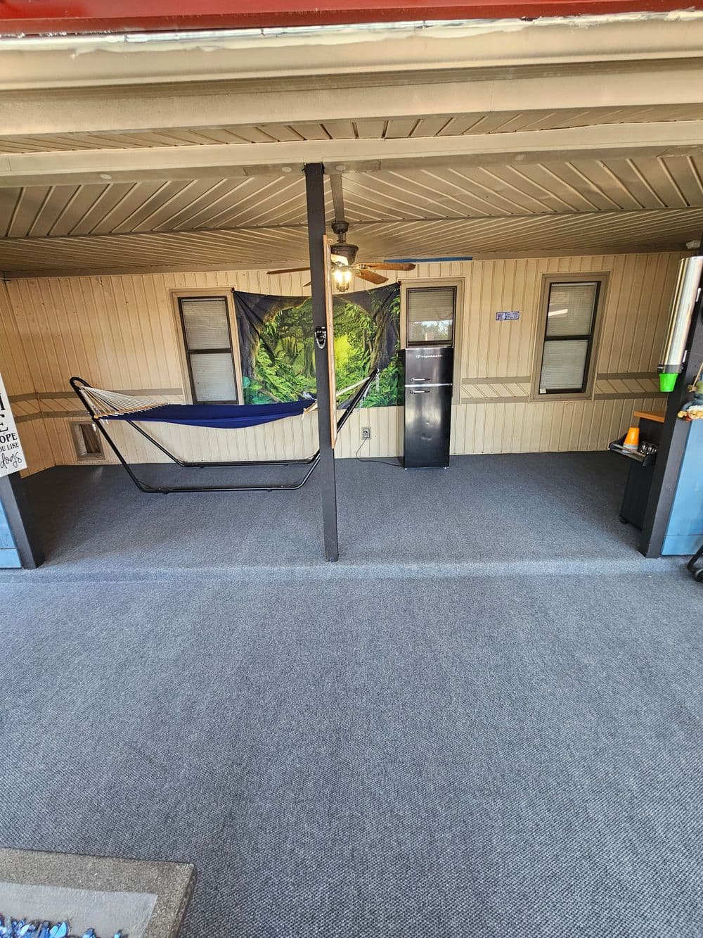 Relaxing porch with a hammock, ceiling fan, and a small refrigerator in a cozy outdoor space.