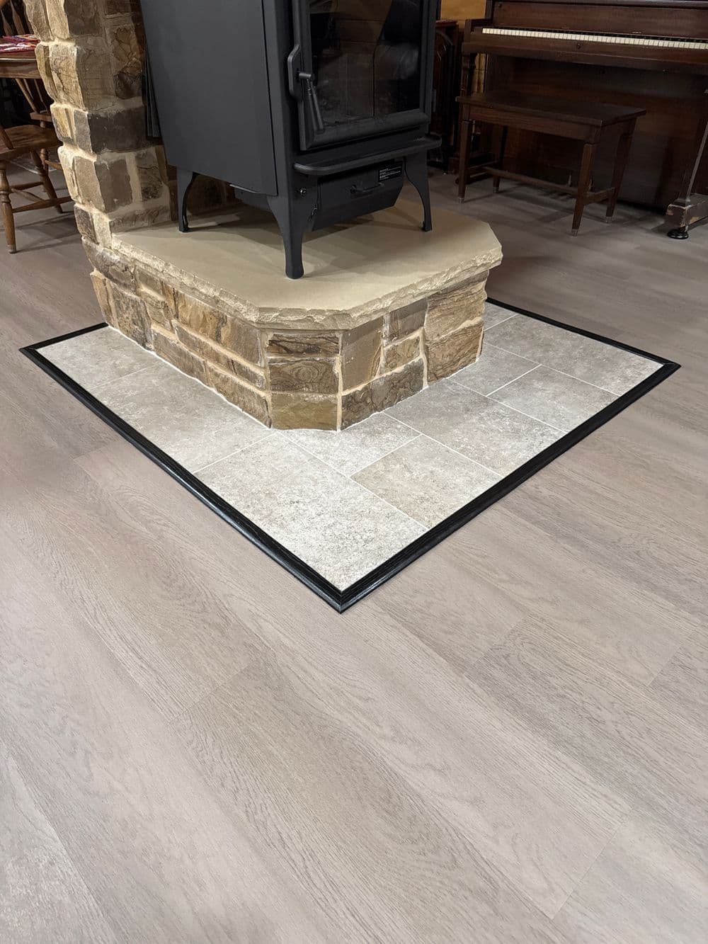 Stone fireplace base surrounded by elegant tile flooring with black trim in cozy interior space.