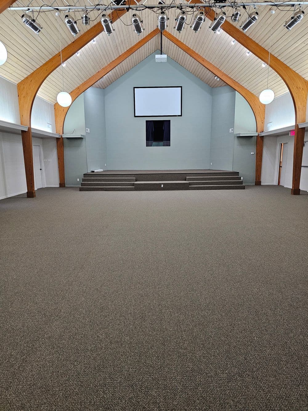 Interior view of a spacious hall with wooden beams, a stage, and modern lighting.