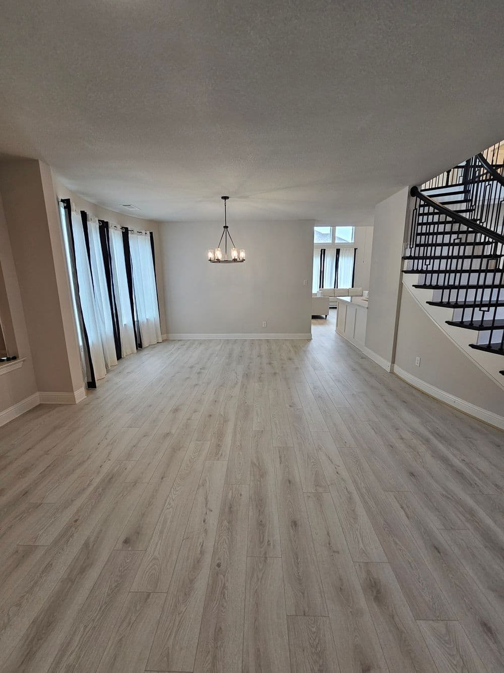 Spacious modern living room with large windows, hardwood floors, and stylish chandelier.