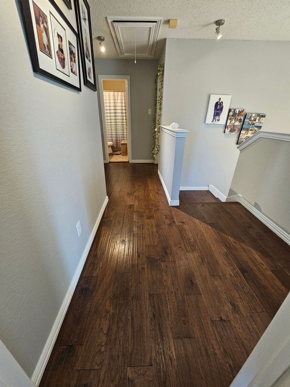 Hallway with wooden floors, framed photos on the wall, leading to a bathroom and staircase.