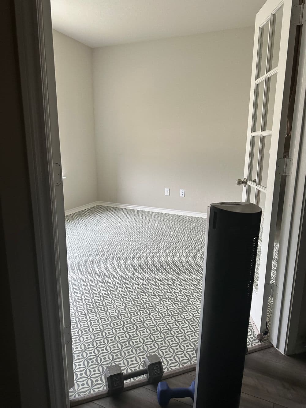 Empty room featuring patterned tile floor, a heater, and dumbbells for fitness activities.
