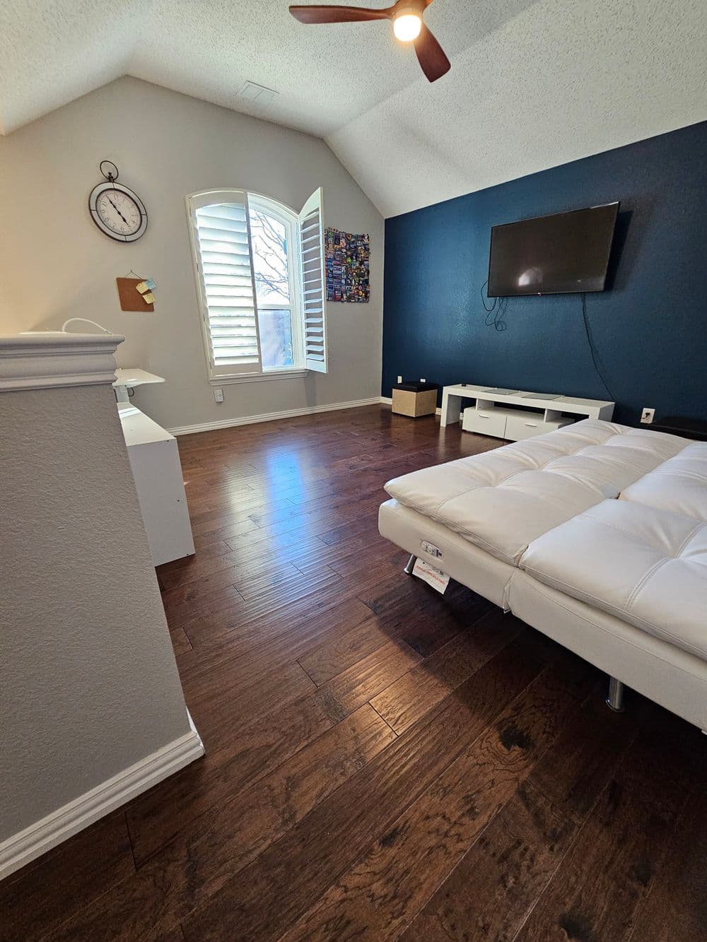 Modern living room with hardwood floors, white furniture, and a dark accent wall.