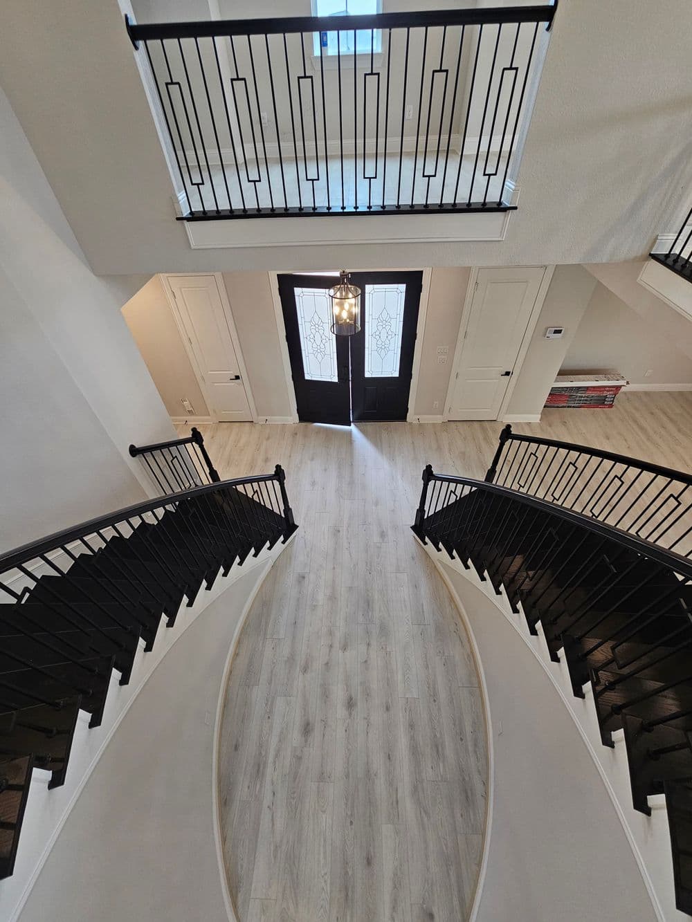Elegant entryway with curved staircase, black railings, and modern light fixture.