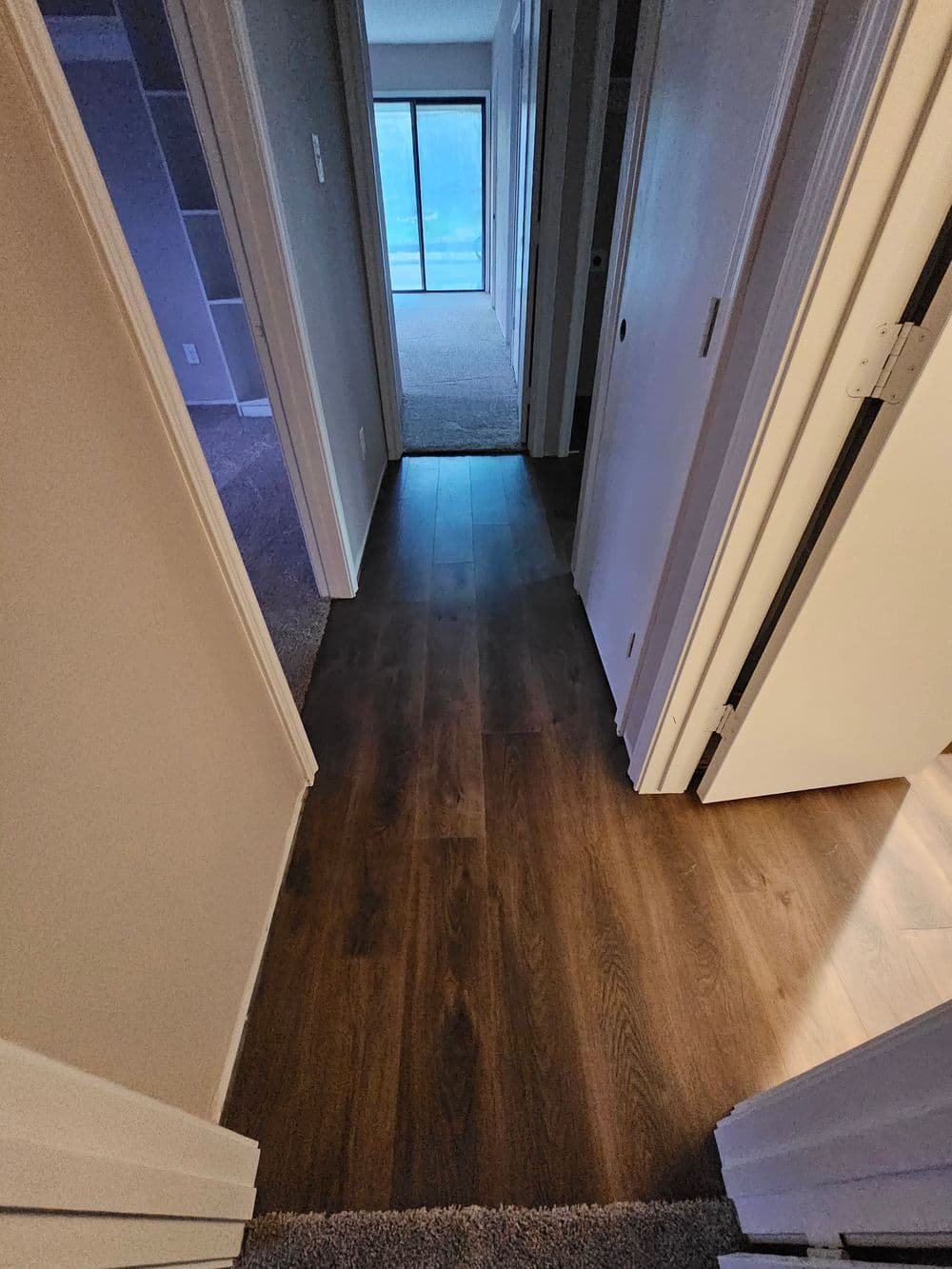 Interior hallway with wooden flooring leading to a bright room and closed doors on either side.