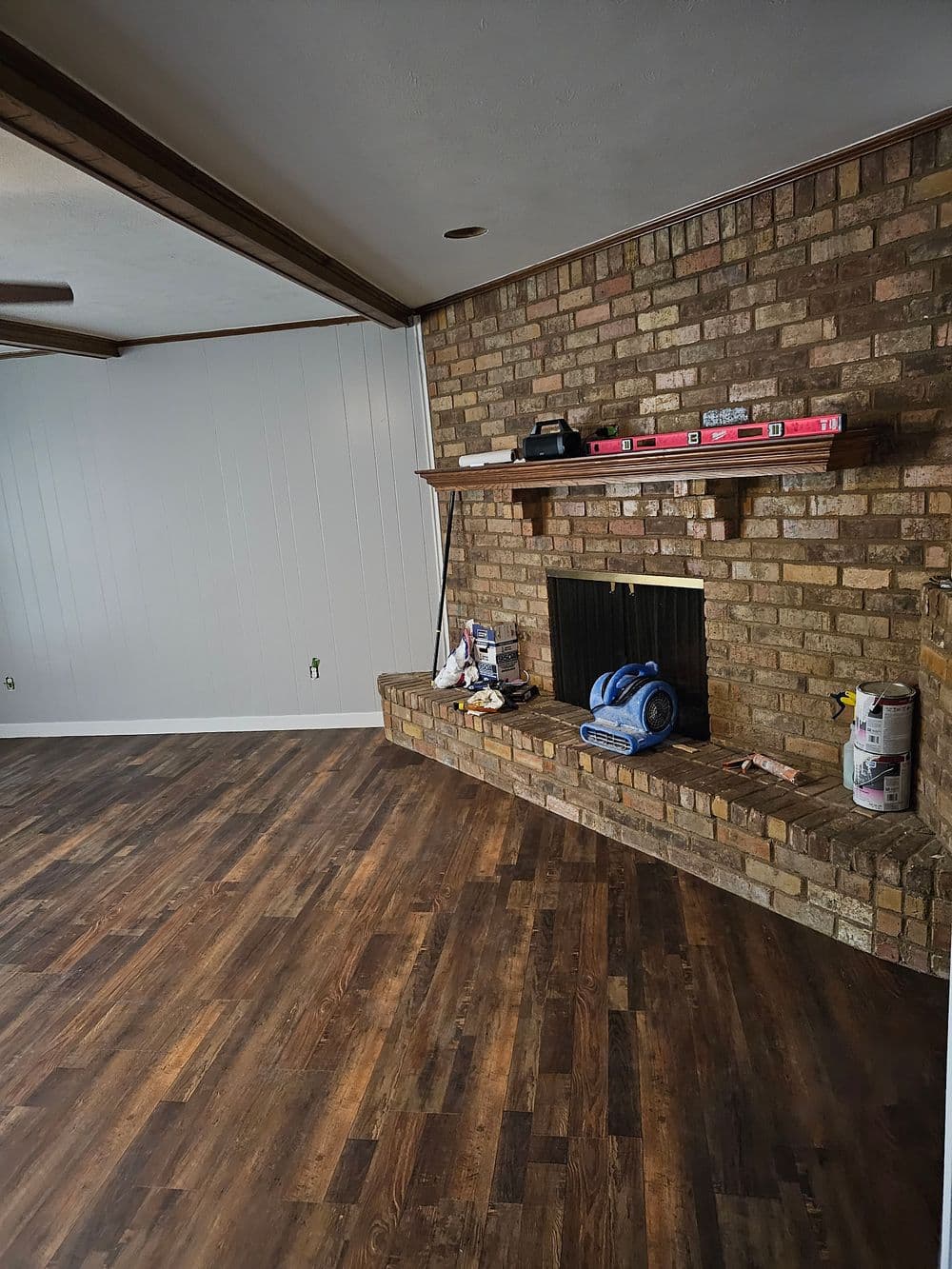 Modern living room with brick fireplace, wooden floor, and construction materials on the shelves.