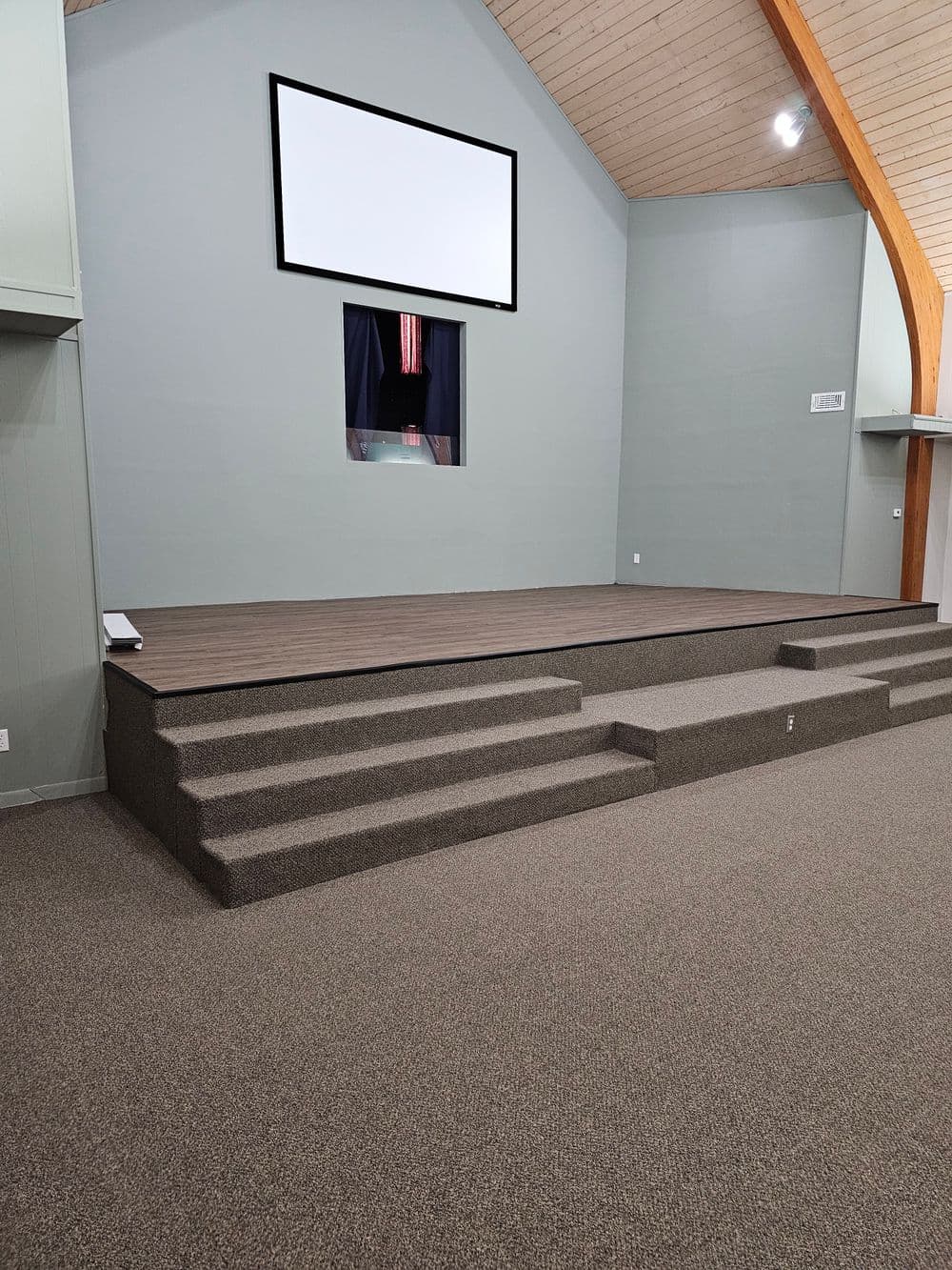 Interior view of a spacious stage with steps, projector screen, and wooden architecture.