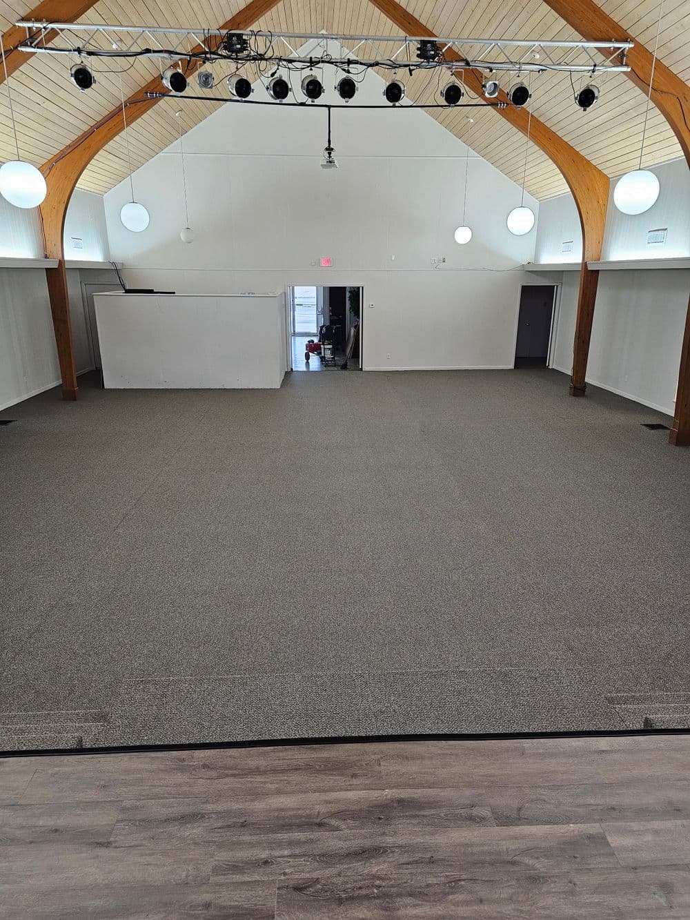 Spacious indoor venue with high ceiling, stage lights, and carpeted flooring.