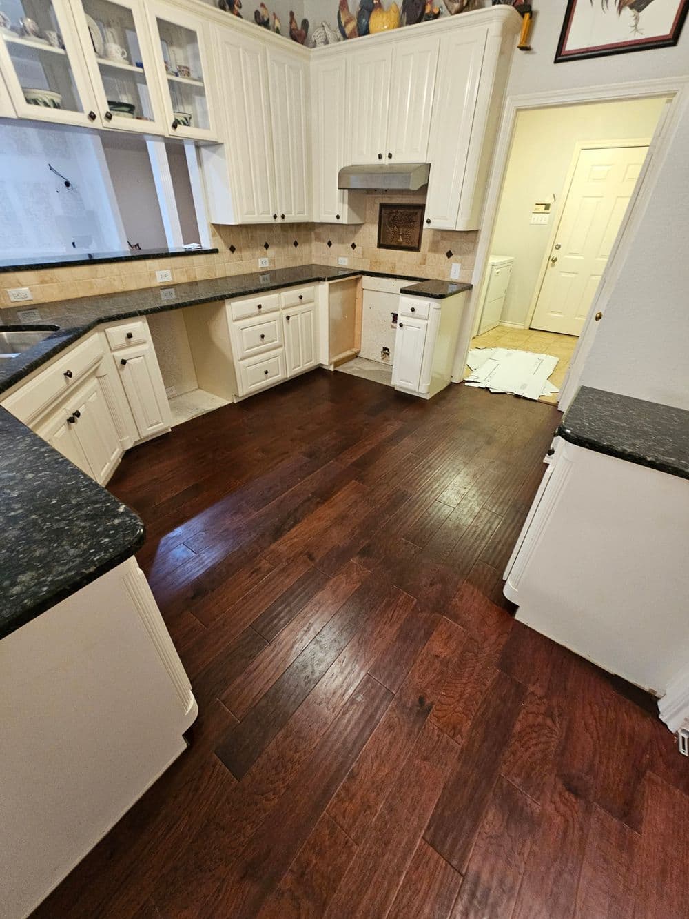 Modern kitchen with dark granite countertops, white cabinets, and hardwood flooring.