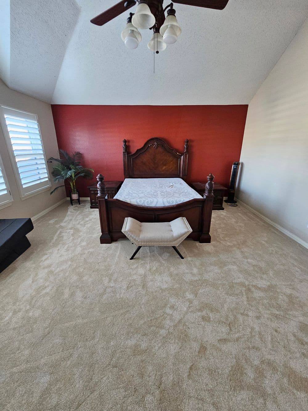 Spacious bedroom with a wooden bed, red accent wall, and plush carpet flooring.