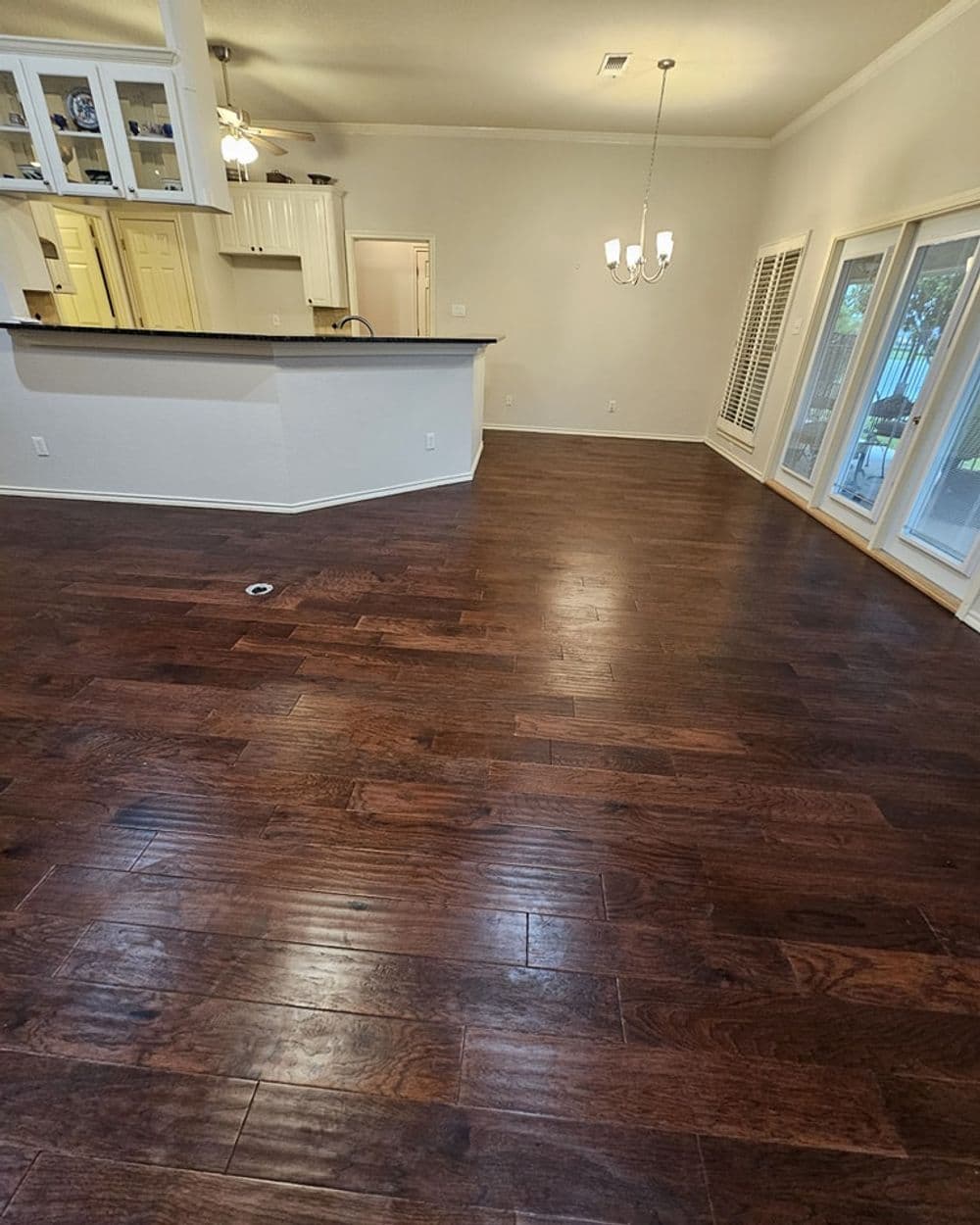 Spacious living room with dark hardwood floors, light walls, and modern kitchen view.