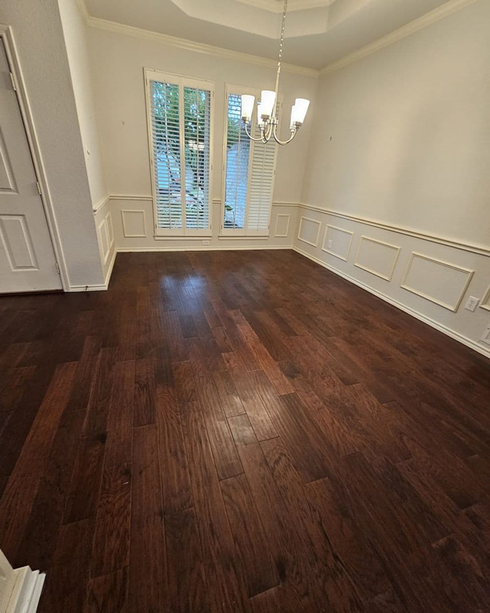 Bright, empty dining room with hardwood flooring and natural light from window shutters.