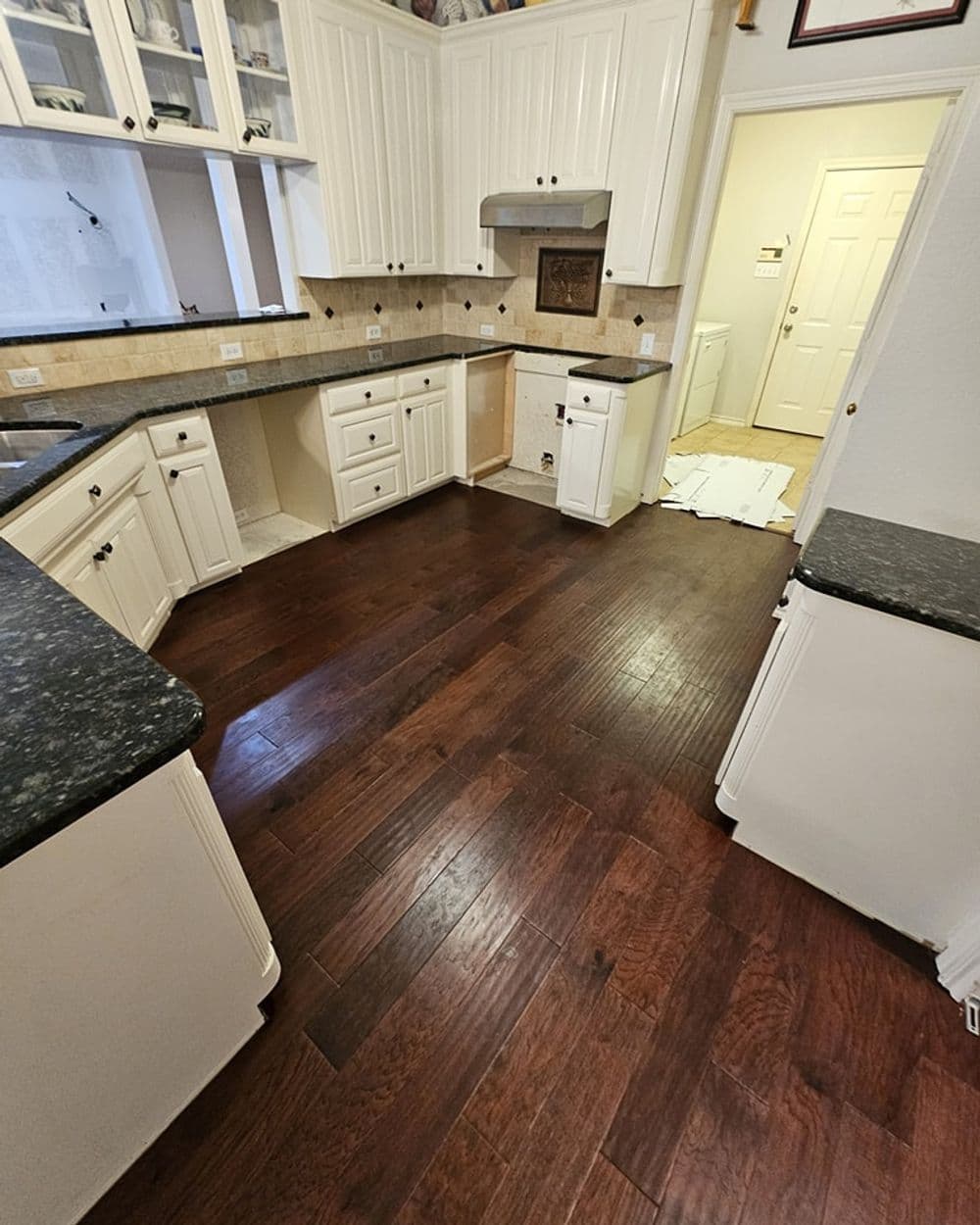 Modern kitchen with dark wood flooring, white cabinets, and granite countertops.