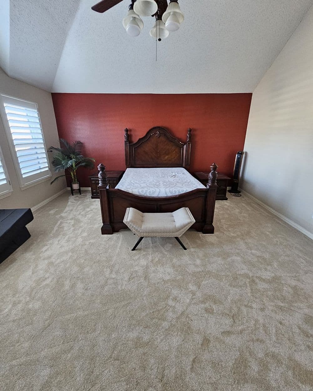 Elegant bedroom with wooden bed and red accent wall, featuring beige carpet and minimal decor.