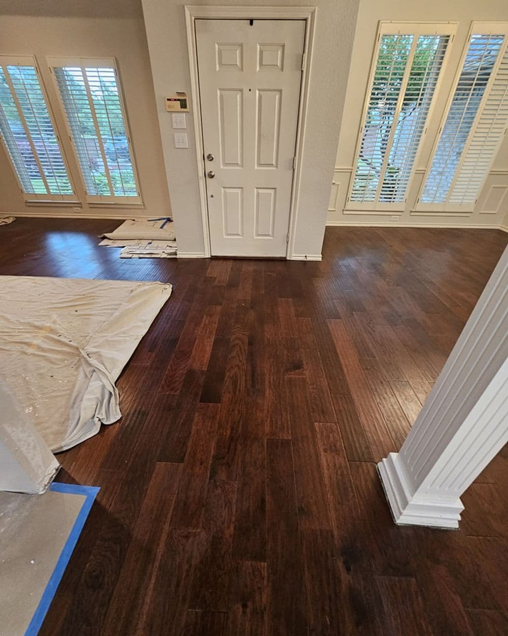 Newly installed dark hardwood flooring in a light-filled entryway with white door and shutters.