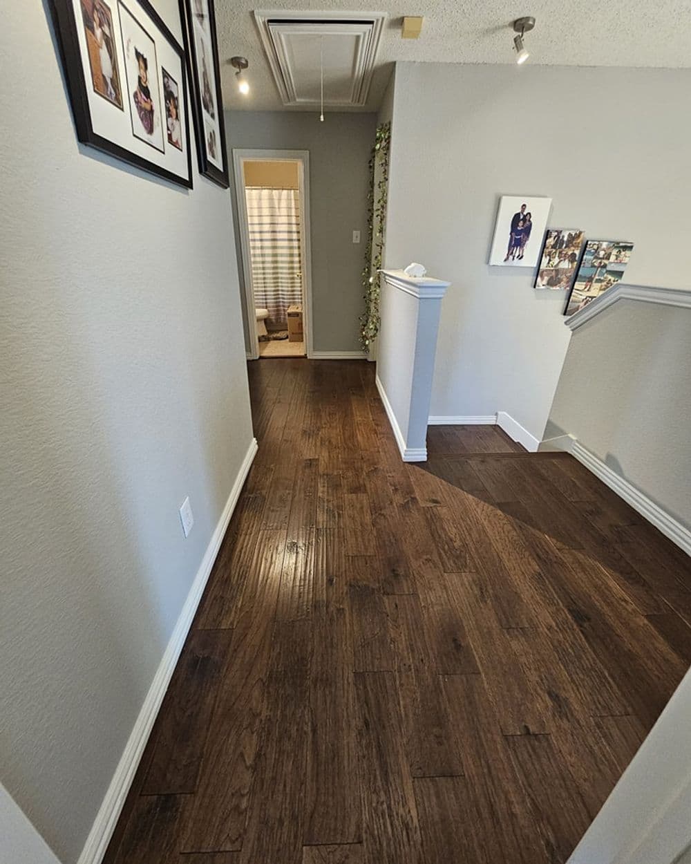 Spacious hallway with wooden flooring and framed photos on the walls. Light-filled corridor.