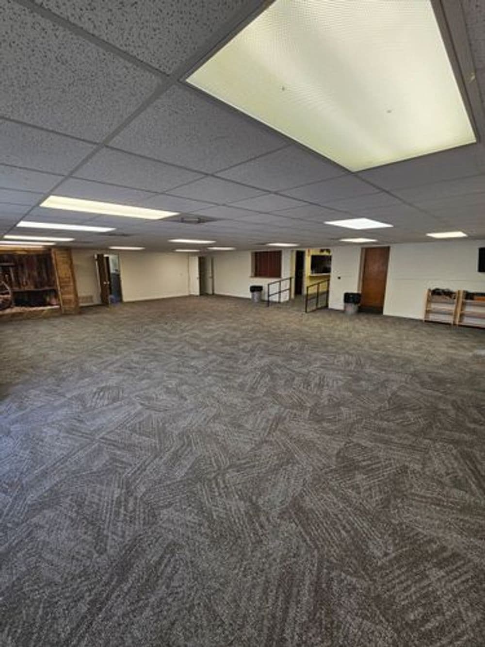 Spacious empty room with patterned carpet, fluorescent lighting, and neutral walls.