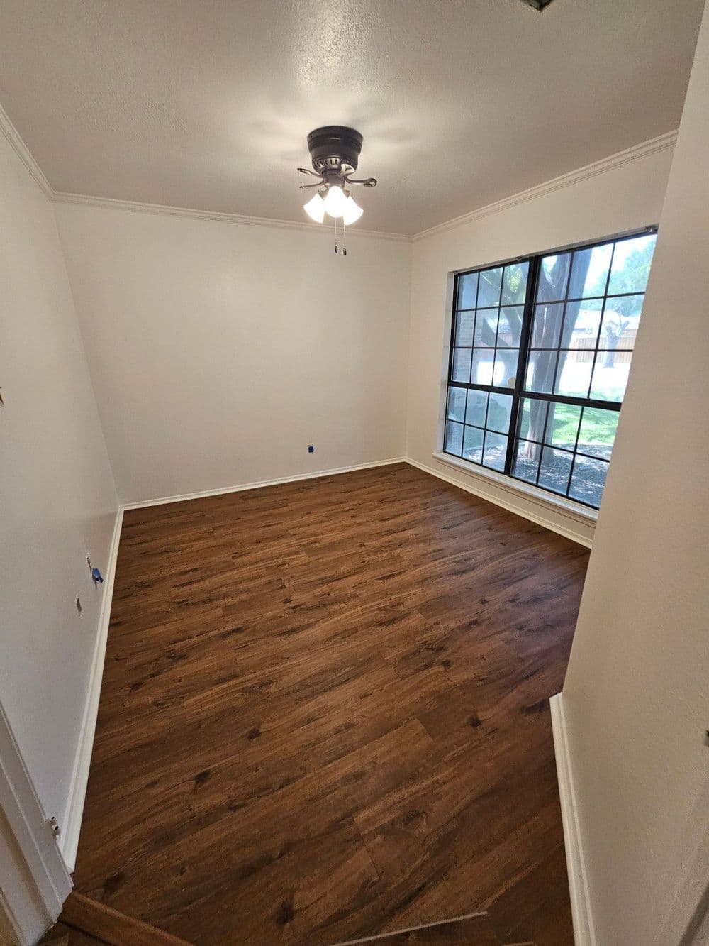 Empty room with wooden flooring, a ceiling fan, and large windows for natural light.