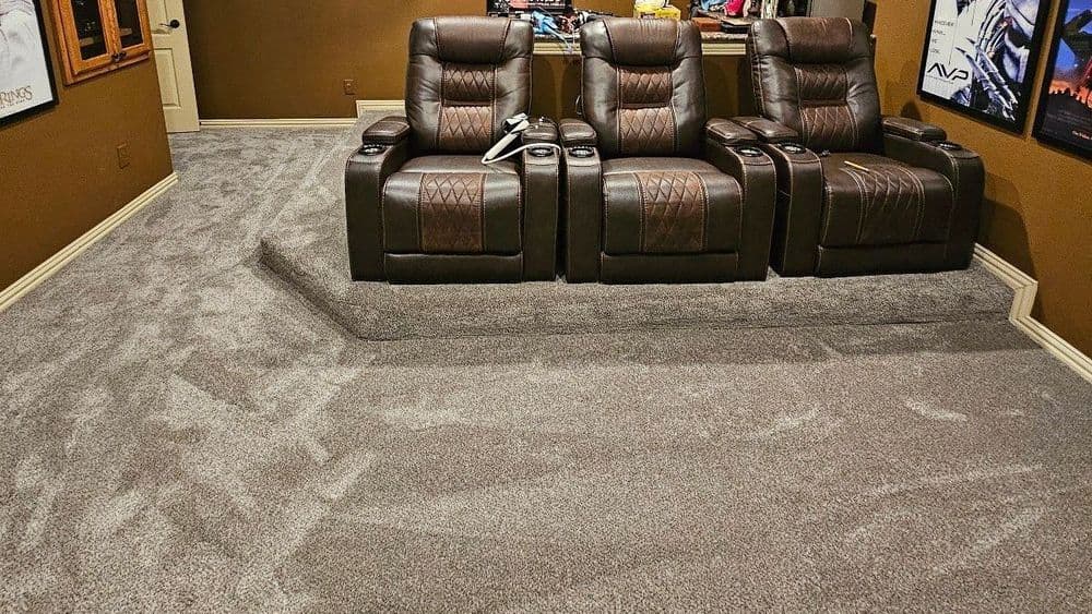 Home theater setup with brown reclining chairs on plush carpet and movie posters on walls.